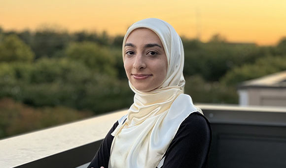 A photo of a woman wearing a hijab standing in front of a sunset