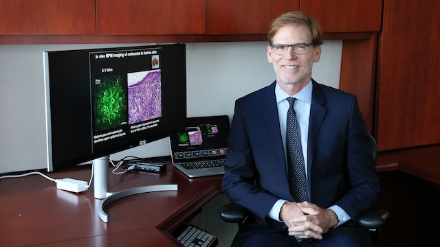 Bruce Tromberg sitting at a desk with screen showing brain scan