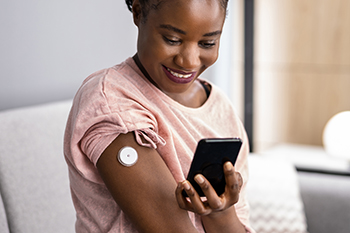 woman testing glucose level with continuous glucose monitor and mobile phone