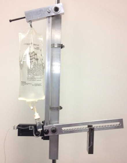 A photo of an IV bag with its cord slightly bent attached to the IV DRIP system, a metal device that is attached to both the top and bottom of the bag.