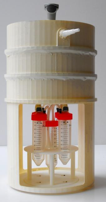 A photo of the microflora refinement system, a white circle with three tubes with red caps attached to the bottom.