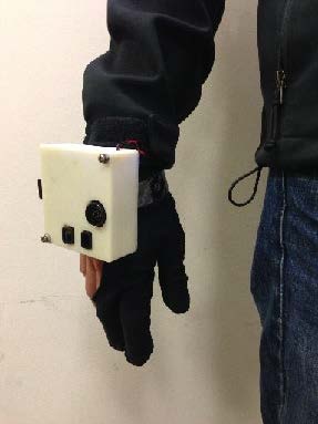 A photo of a gloved hand with a white box attached to the back. 