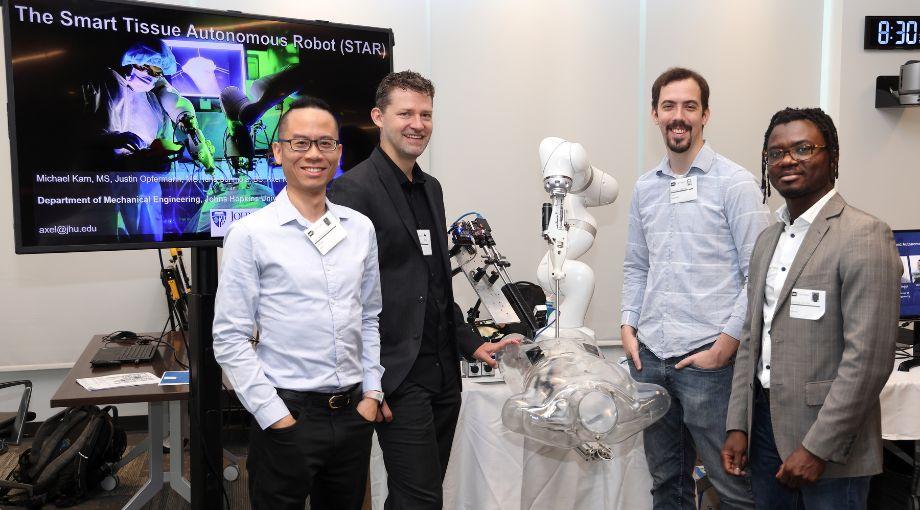 A group from Johns Hopkins University stands with their surgical robotic system called STAR (for Smart Tissue Autonomous Robot). L-R: Michael Kam, Axel Krieger, Justin Opfermann, and Idris Sunmola.